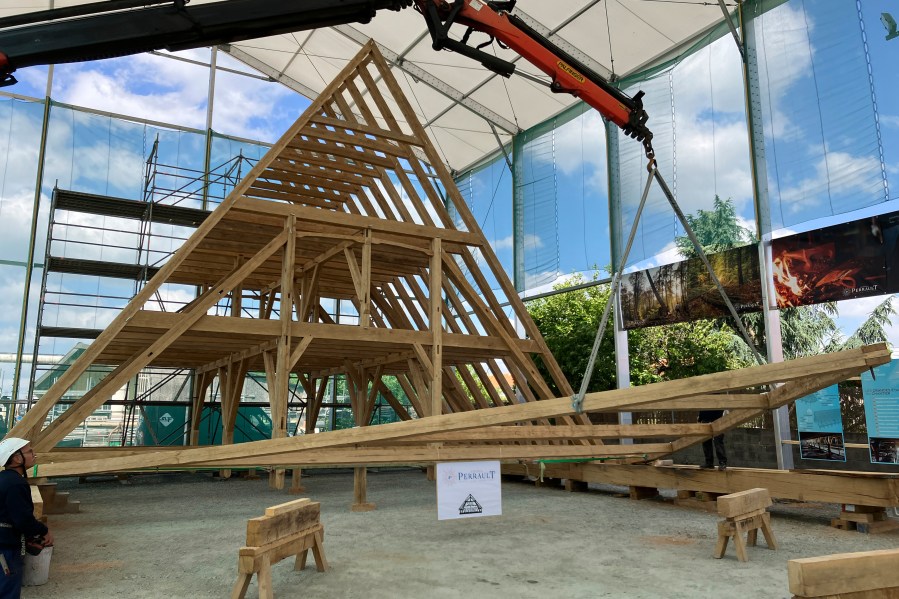 A crane lifts a part of the new roof of the Notre Dame de Paris cathedral, Thursday, May 25, 2023, near Angers, western France. Carpenters building a new timber frame for the fire-ravaged roof of Paris' Notre Dame Cathedral are using the same tools and techniques as their medieval predecessors. For them, working with hand-axes to fashion oak beams has been like stepping back in time. (AP Photo/Jeffrey Schaeffer)
