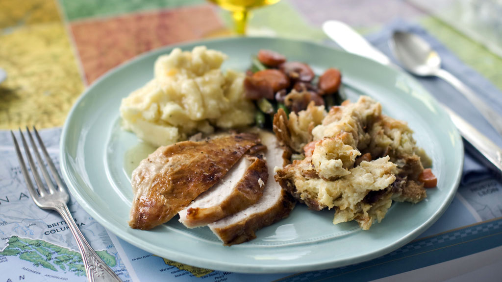 A plate of roasted turkey and gravy, stuffing, mashed potatoes, and glazed carrots is pictured.