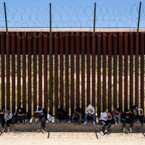 Migrants sit by an iron fence in San Diego, California on June 13, 2024.