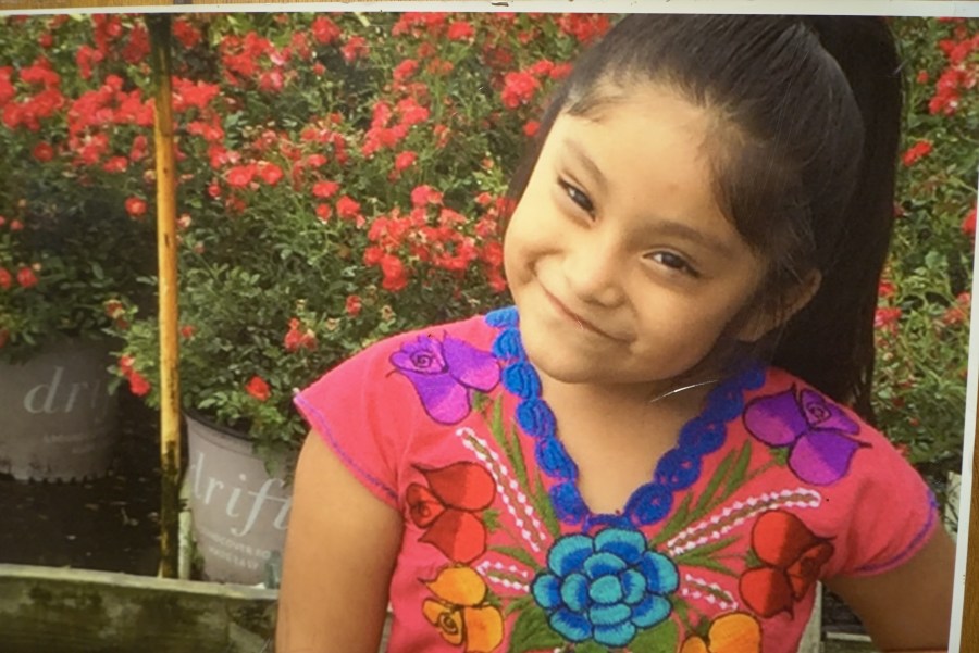A smiling Hispanic girl sitting outside.