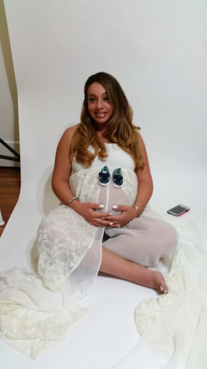 A dark-haired woman in a white sheet doing a maternity photo shoot.