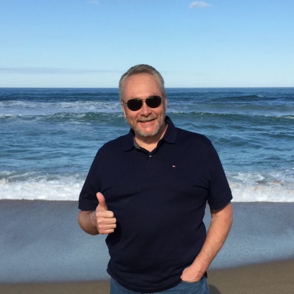 An older man on a beach giving a thumbs up.