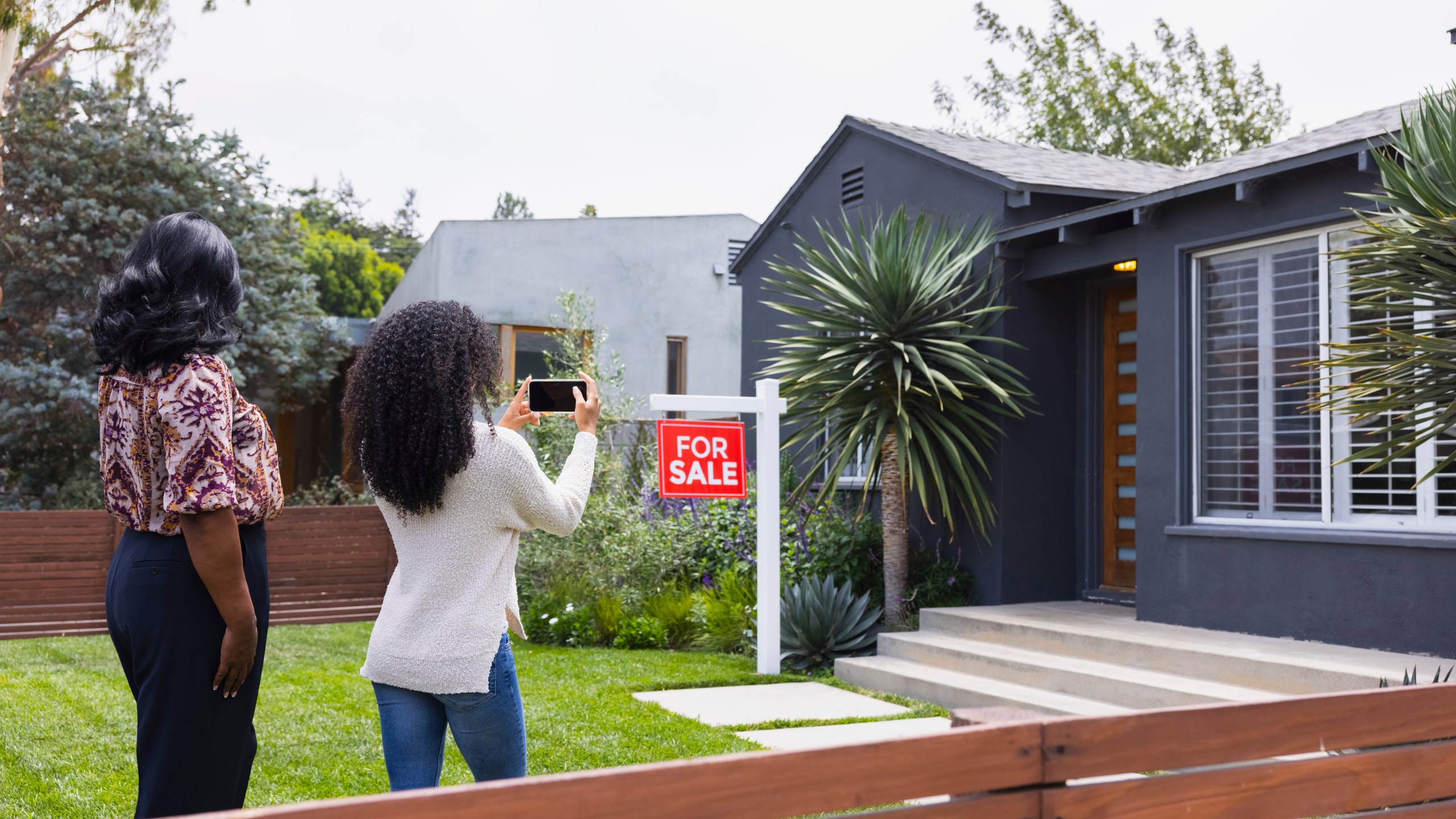 Young woman photographing house through mobile phone with mother.