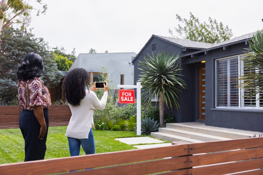 Young woman photographing house through mobile phone with mother.