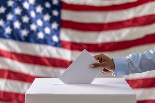 A hand casts a vote in a ballot box.