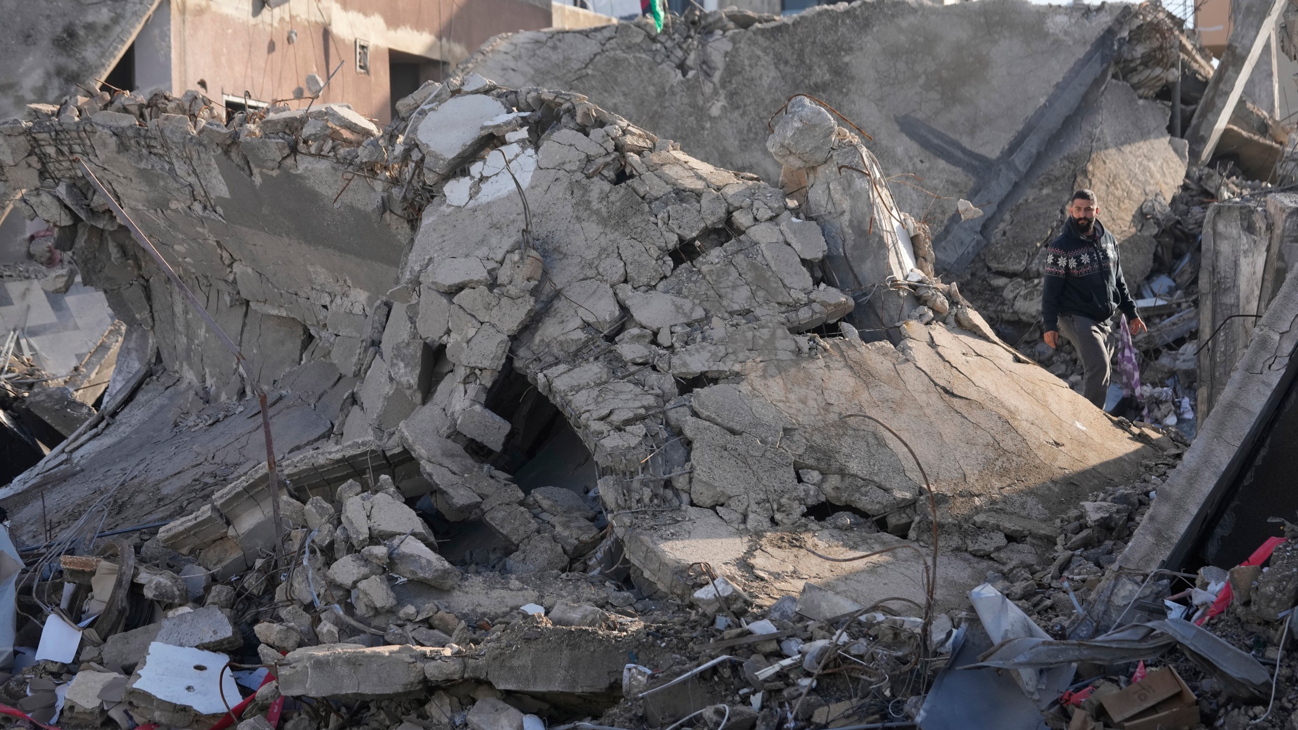 A man stands on the rubble of a destroyed building that housed his apartment in Tyre, southern Lebanon, Thursday, Nov. 28, 2024. (AP Photo/Hussein Malla)