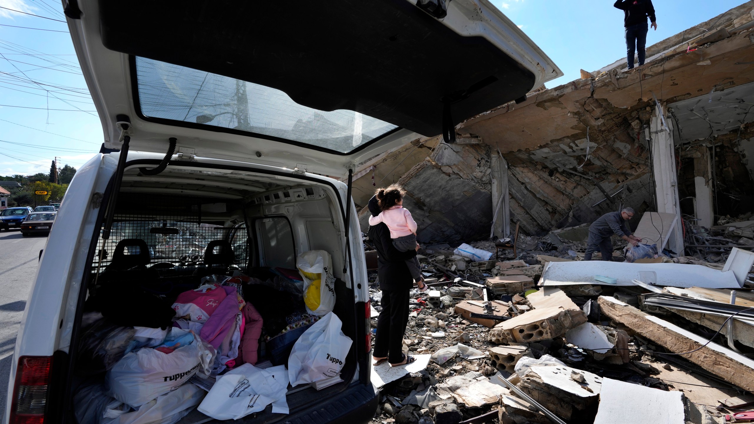 Safaa Haidous, carries her daughter Yara, 4, as she speaks with her husband Rawad Srour, who is stands on the roof of their family destroyed house, as they collect the remains of their belongings after they returned to Hanouiyeh village, southern Lebanon, Thursday, Nov. 28, 2024 following a ceasefire between Israel and Hezbollah that went into effect on Wednesday.(AP Photo/Hussein Malla)