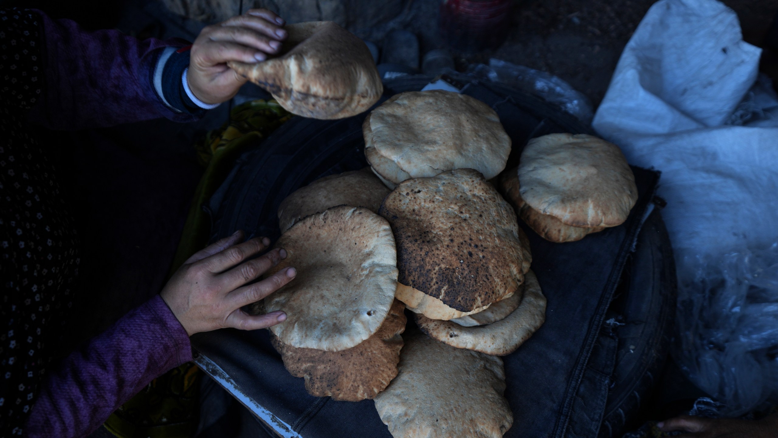 A Palestinian woman sorts through fresh bread amid dire food shortages in Deir al-Balah, Gaza Strip, Monday, Dec. 2, 2024. (AP Photo/Abdel Kareem Hana)