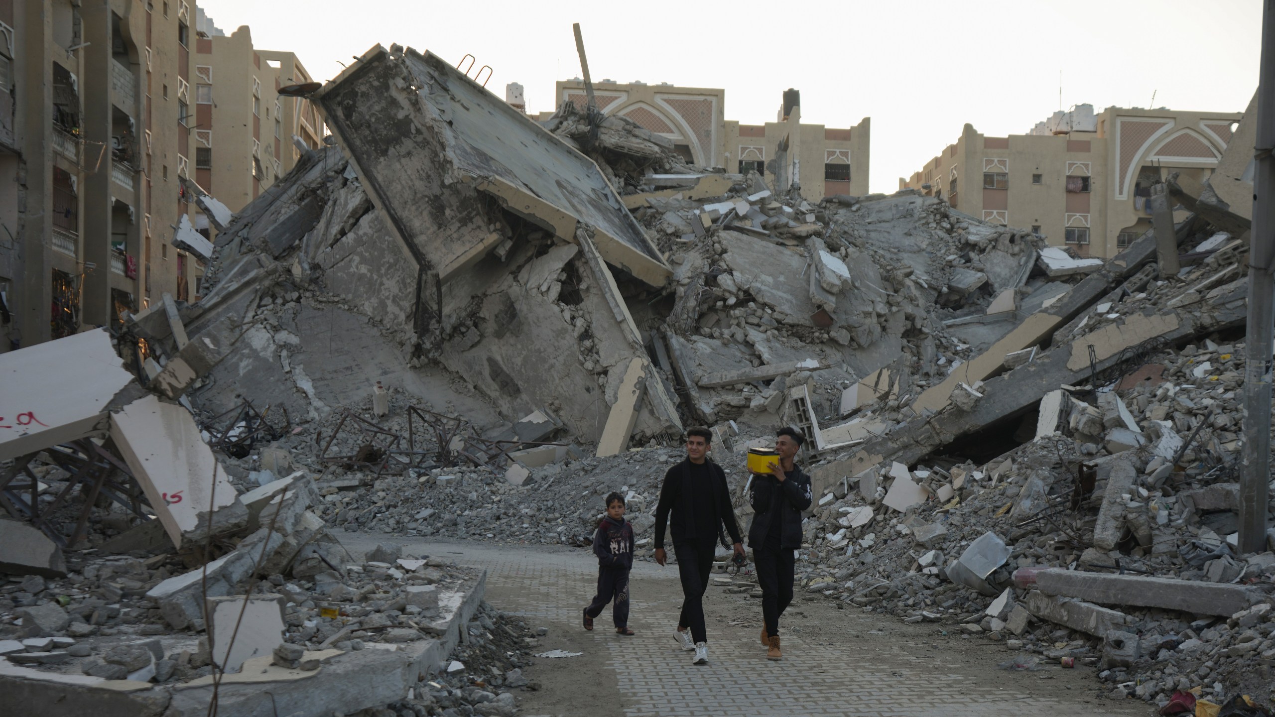 Young Palestinians walk amongst rubble of destroyed buildings at a neighbourhood in Khan Younis, Gaza Strip, Sunday, Dec. 1, 2024. (AP Photo/Abdel Kareem Hana)