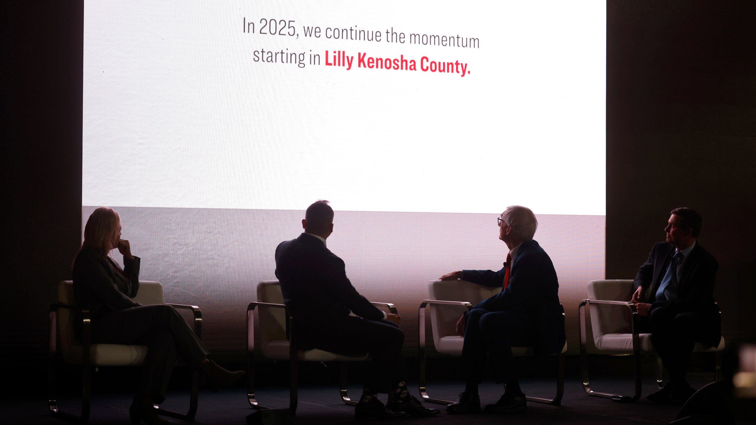 Kenosha County Executive Samantha Kerkman, from left, Edgardo Hernandez, executive vice president and president of Lilly manufacturing operations, Gov. Tony Evers, and David Ricks, chair and CEO of Eli Lilly, watch a video during the announcement that Eli Lilly is expanding in Wisconsin Thursday, Dec. 5, 2024, in Kenosha, Wis. (Sean Krajacic/The Kenosha News via AP)