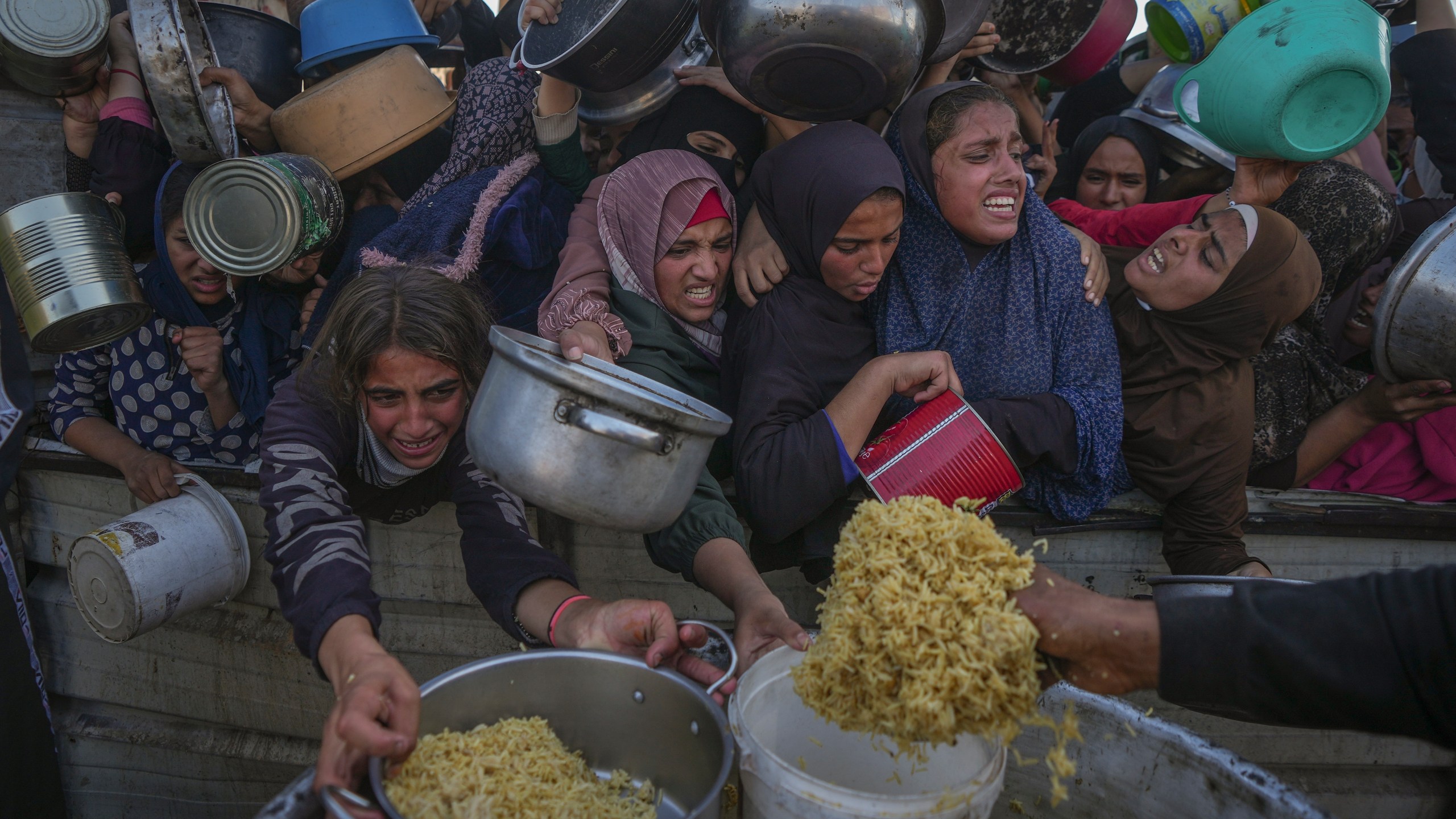 Palestinian girls struggle as they get donated food at a distribution center in Khan Younis, Gaza Strip, on Friday, Dec. 6, 2024. (AP Photo/Abdel Kareem Hana)