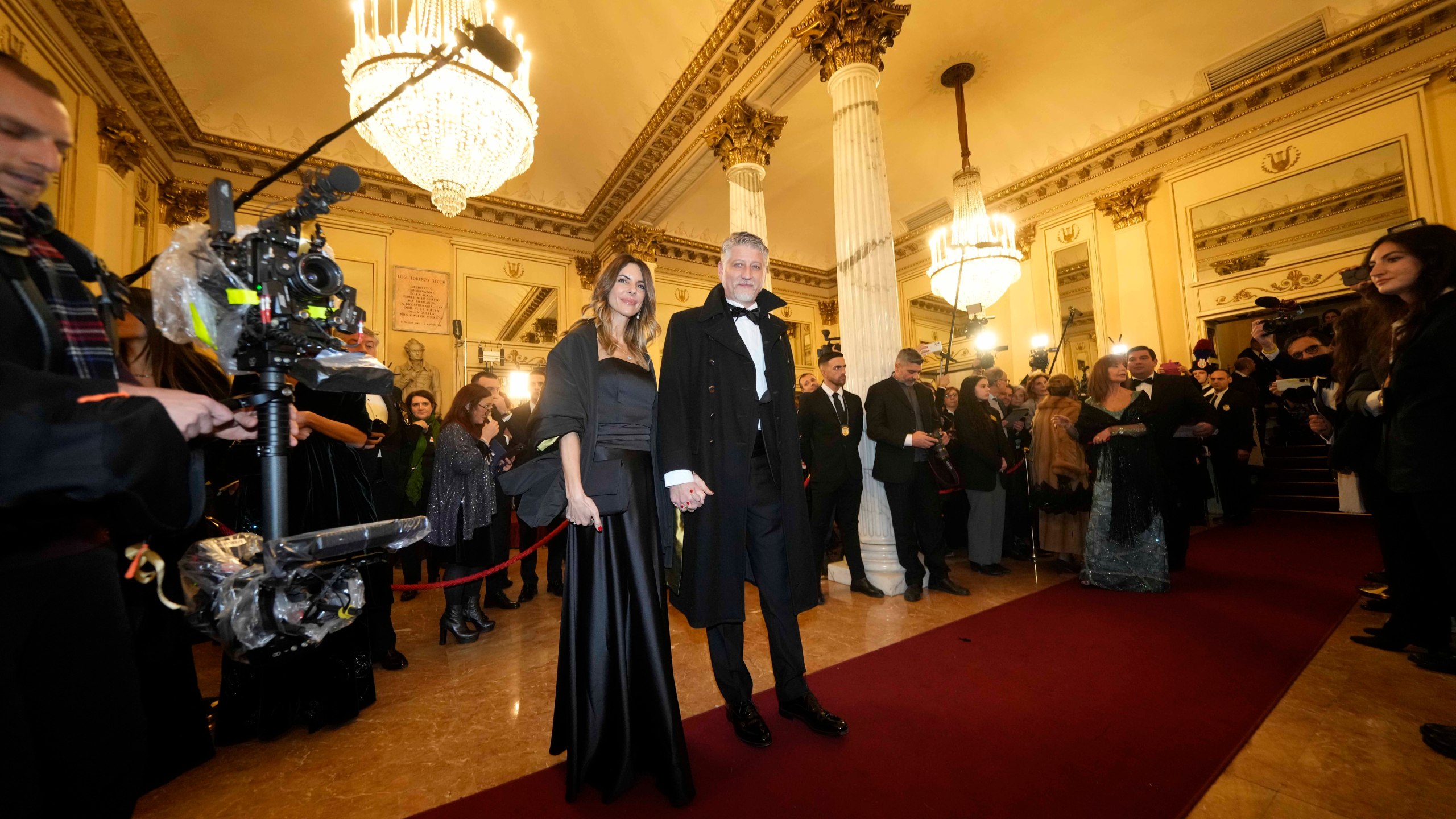 Italian Culture Minister Alessandro Giuli is flanked by his wife Valeria Falcioni as they arrive at Milan's Opera House La Scala, Italy, for the opening of the 2024-25 season featuring Giuseppe Verdi's 'La Forza del destino', Saturday, Dec. 7, 2024. (AP Photo/Luca Bruno)